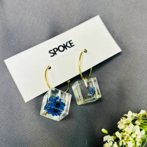 : A close-up image of the Natural Flower Resin Reserved Earring showcases the intricate floral design encased in transparent resin. The vibrant colors of the flower pop against the backdrop of the resin pendant, creating a visually stunning piece of jewelry.